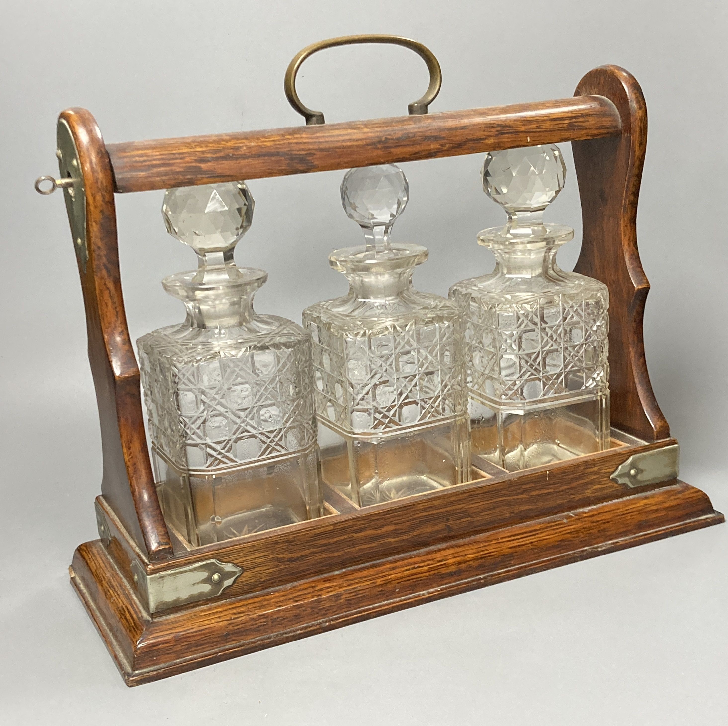 An Edwardian oak three decanter tantalus